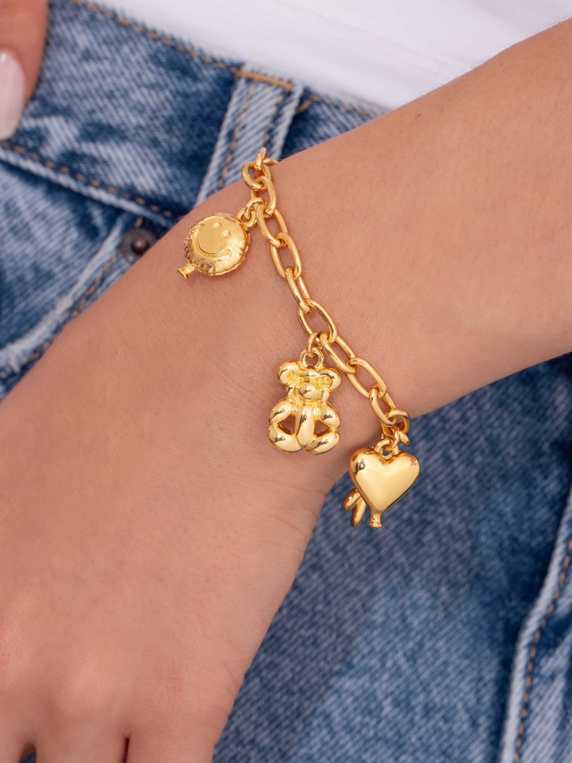 Gold anklet with charms on a person's wrist against a denim background
