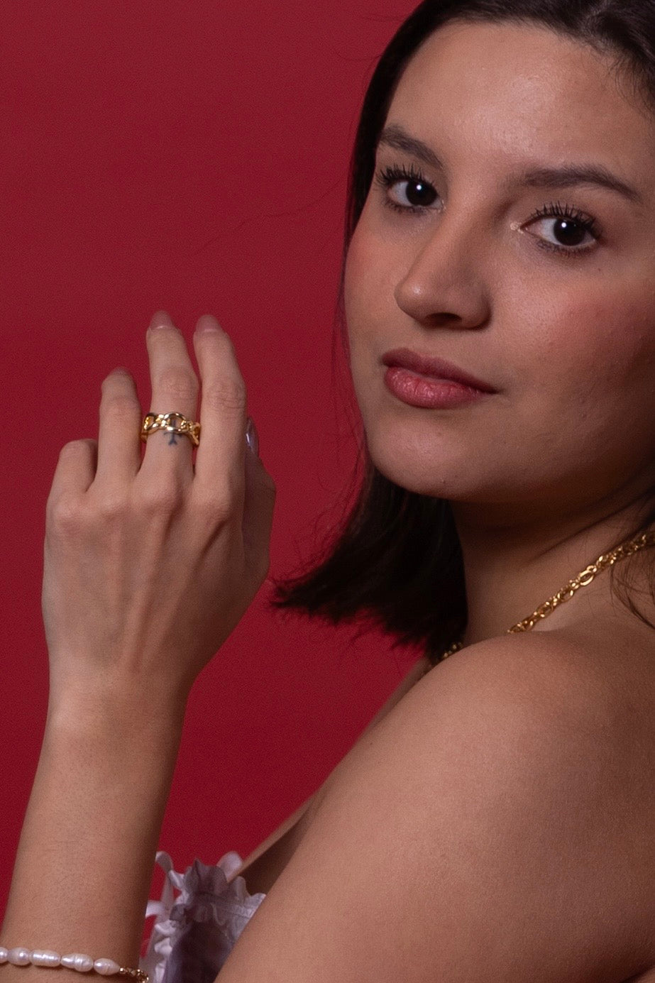 Woman wearing a 14k gold plated ring and necklace against a red background