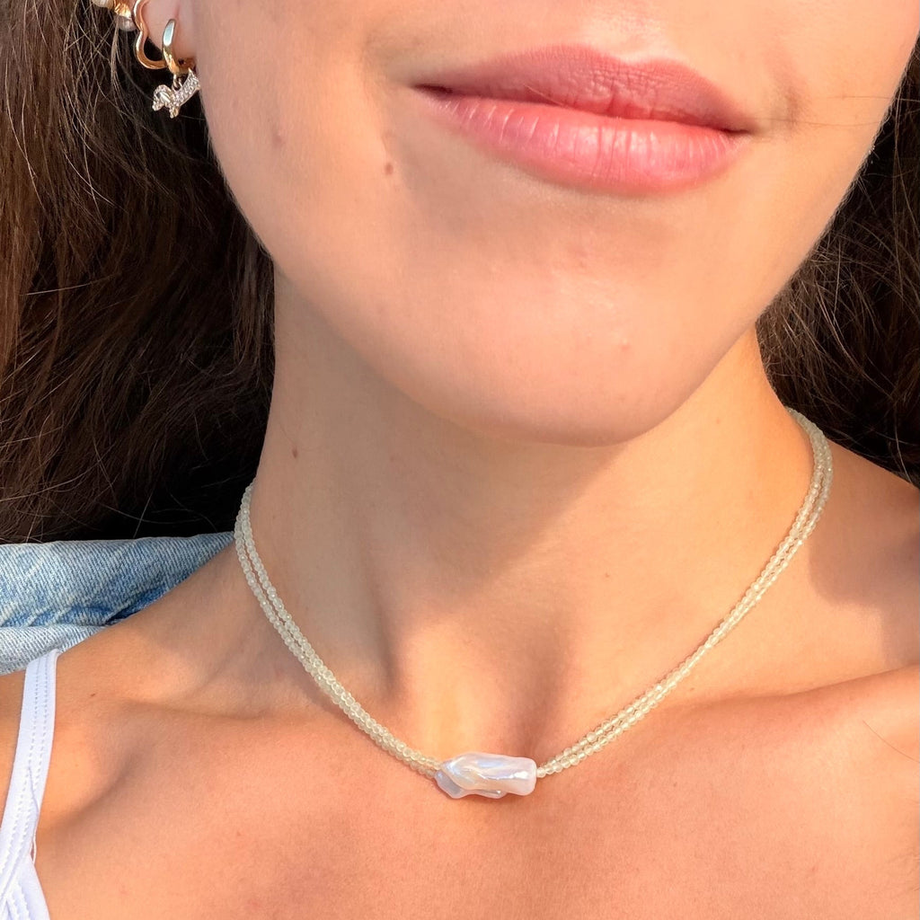 Close-up of a person wearing a delicate necklace with a clear stone.